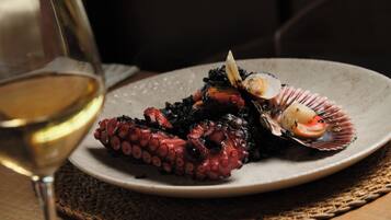 Un plato de pulpo con una concha de vieira, una copa de vino blanco y un mantel tejido.