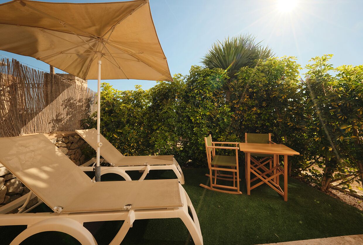 Une terrasse avec des chaises longues et une table, entourée de verdure et d’une clôture en bambou.