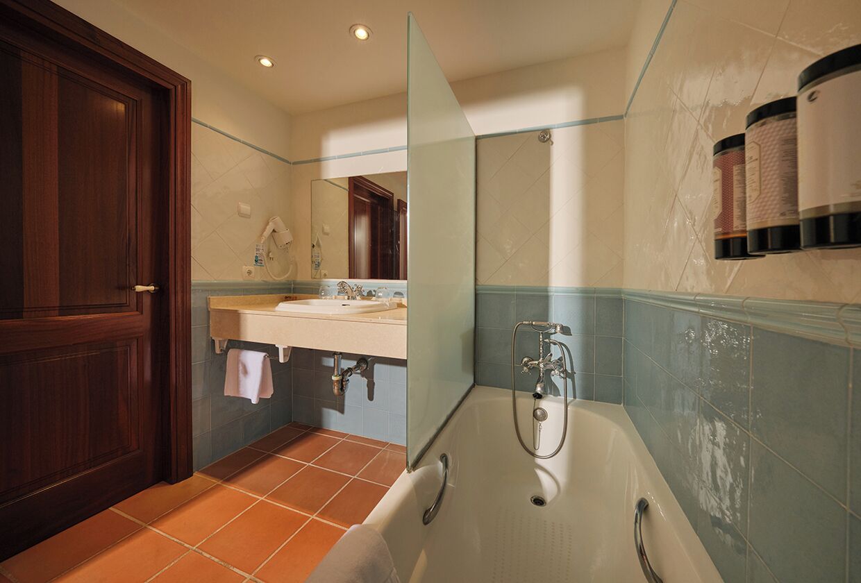 A bathroom with a wooden door, a sink, a mirror, a bathtub, and toiletries on the wall.
