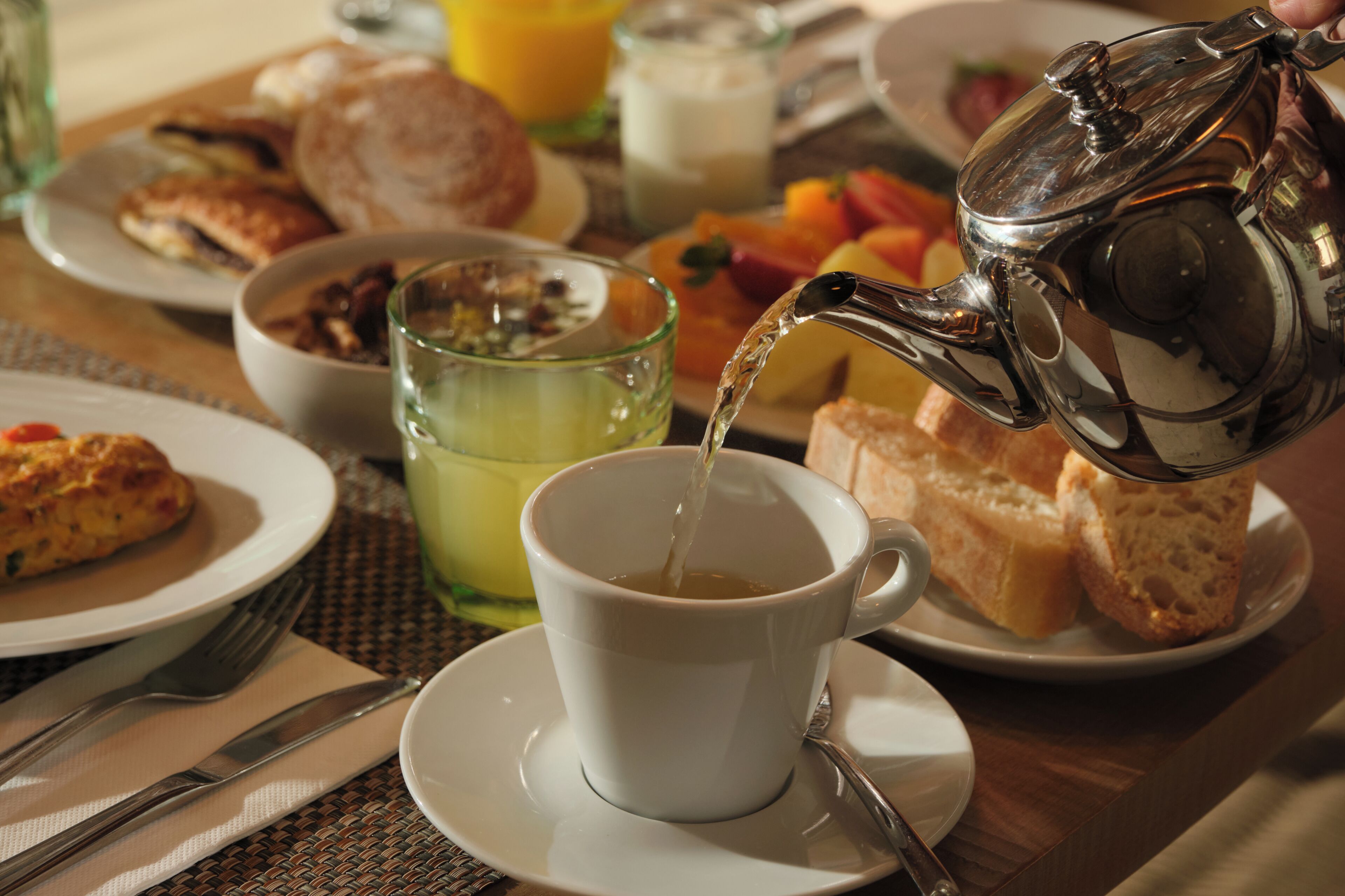 Een ontbijtsetting met een kop thee, toast, fruit en een glas sap op een tafel.