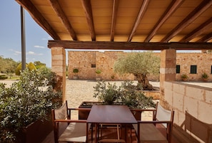 An outdoor patio with a wooden pergola, stone walls, and potted plants. - Hotel Rural Es Riquers (Porreres)