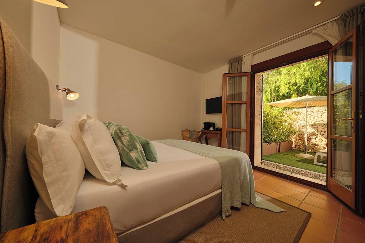 A bedroom with a bed, a television, a small table, and a view of an outdoor garden through a glass door.