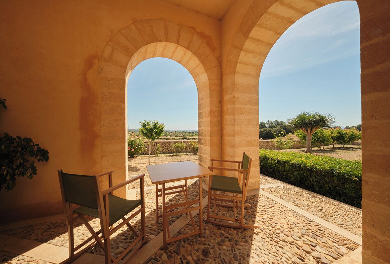 Un espace extérieur aménagé, abrité et doté d’une table et de chaises, d’un sol en pierre et d’une vue sur un jardin paysager.
