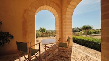 Un espace extérieur aménagé, abrité et doté d’une table et de chaises, d’un sol en pierre et d’une vue sur un jardin paysager.