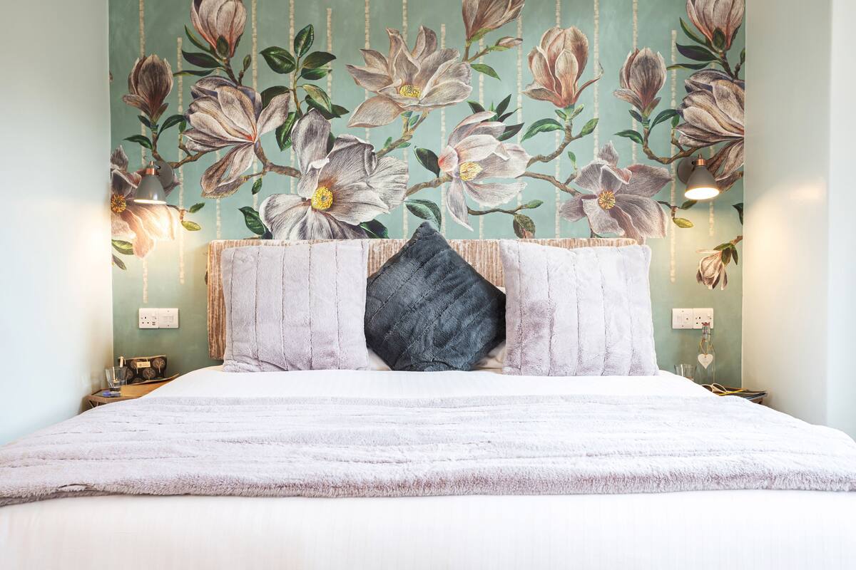 A bed with a white duvet and a dark pillow, a wall with floral wallpaper, and two bedside lamps.