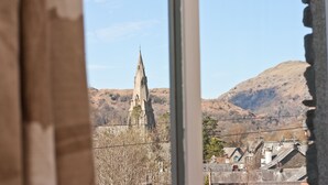 A view through a window of a church with a tall spire, surrounded by hills and buildings. - Elder Grove (Ambleside)