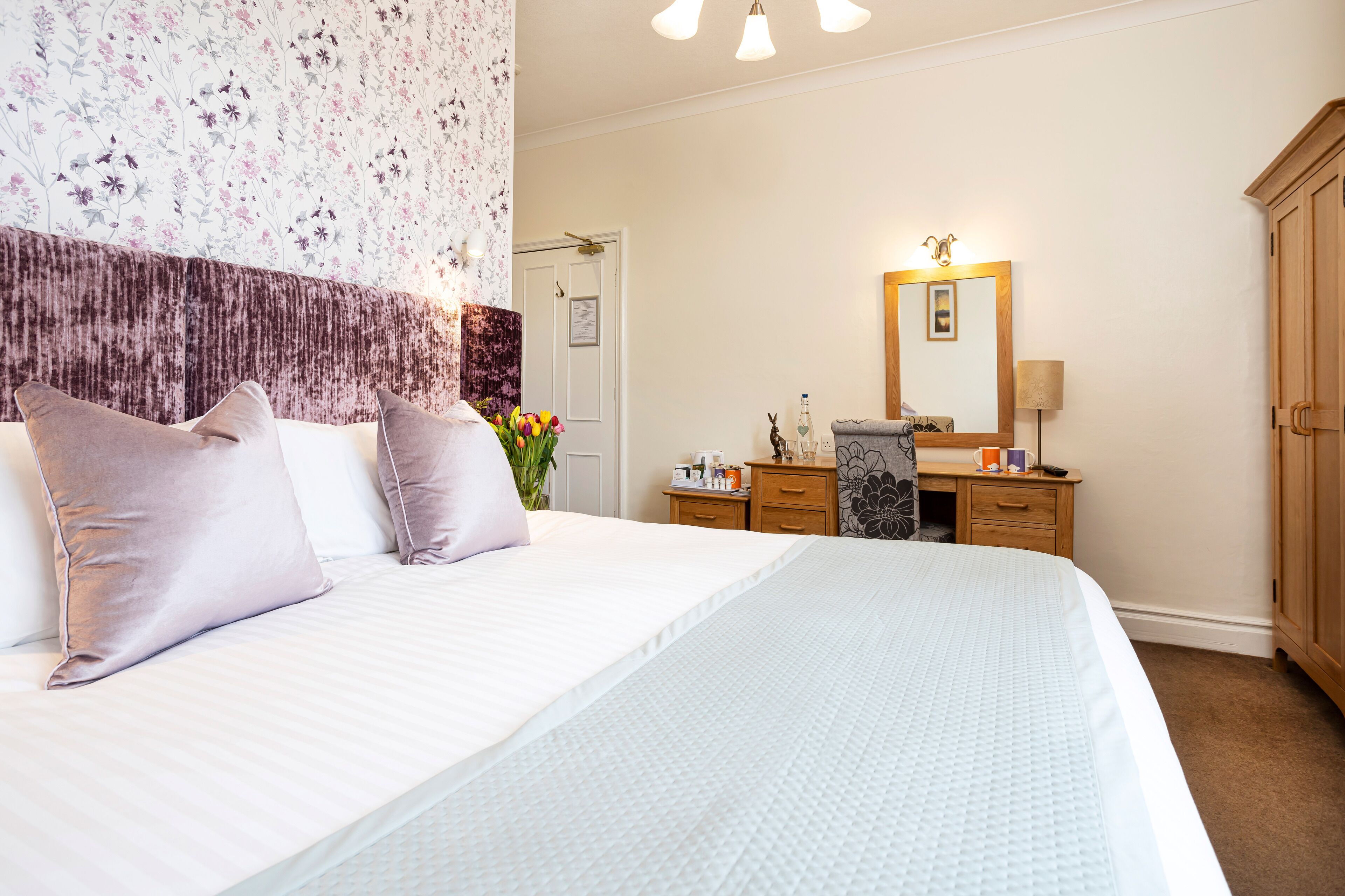 A hotel room with a large bed, a wooden dresser, a mirror, and a door.