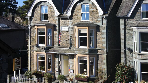A two-story stone building with a traditional architectural style, featuring multiple windows and a flag. - Elder Grove (Ambleside)