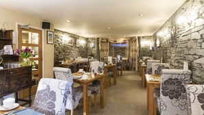 A dining area with wooden tables and chairs, stone walls, and a view of the outdoors. - Elder Grove (Ambleside)