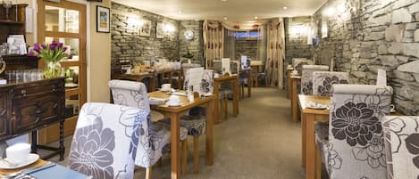 A dining area with wooden tables and chairs, stone walls, and a view of the outdoors.