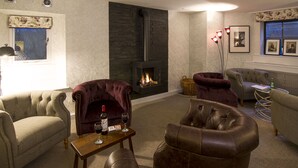 A cozy living room with a fireplace, plush seating, and a small table with a bottle and glasses. - Elder Grove (Ambleside)