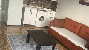 A compact living space with a sofa, a coffee table, a washing machine, and a refrigerator. - Oguz Pansiyon (Denizli)