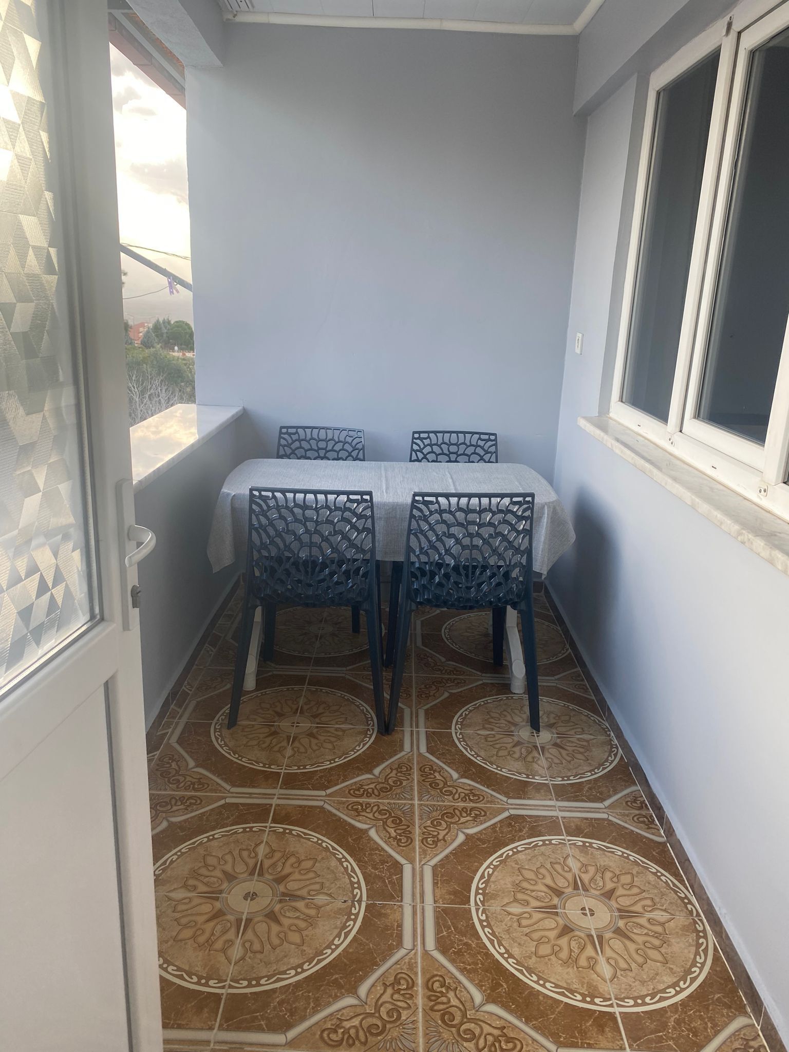 Un pequeño balcón con una mesa, sillas, una ventana y baldosas de suelo con diseños.