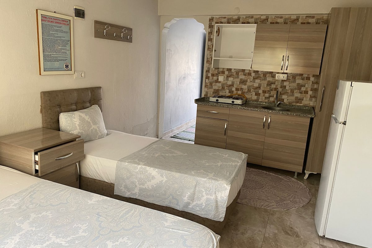 A hotel room with two beds, a kitchenette, and a bathroom.