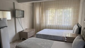 A bedroom with two beds, a TV mounted on the wall, and a refrigerator. - Oguz Pansiyon (Denizli)