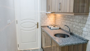 A compact kitchen with a built-in gas stove, a sink, and wooden cabinets. - Oguz Pansiyon (Denizli)