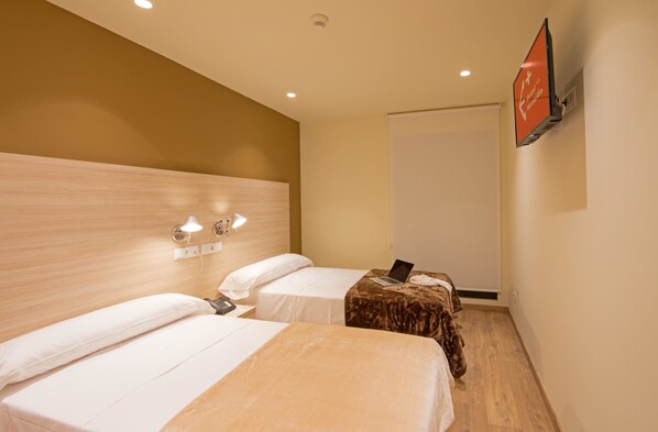 A hotel room with two beds, a TV mounted on the wall, and a wooden headboard. - Hotel Hormilla (Hormilla)