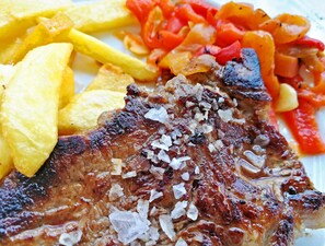 Un steak assaisonné de sel et de poivre, servi avec des frites et des légumes grillés.