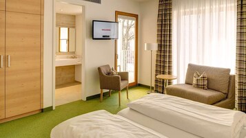 A hotel room with two beds, a sofa, a chair, a TV, and a window with curtains.