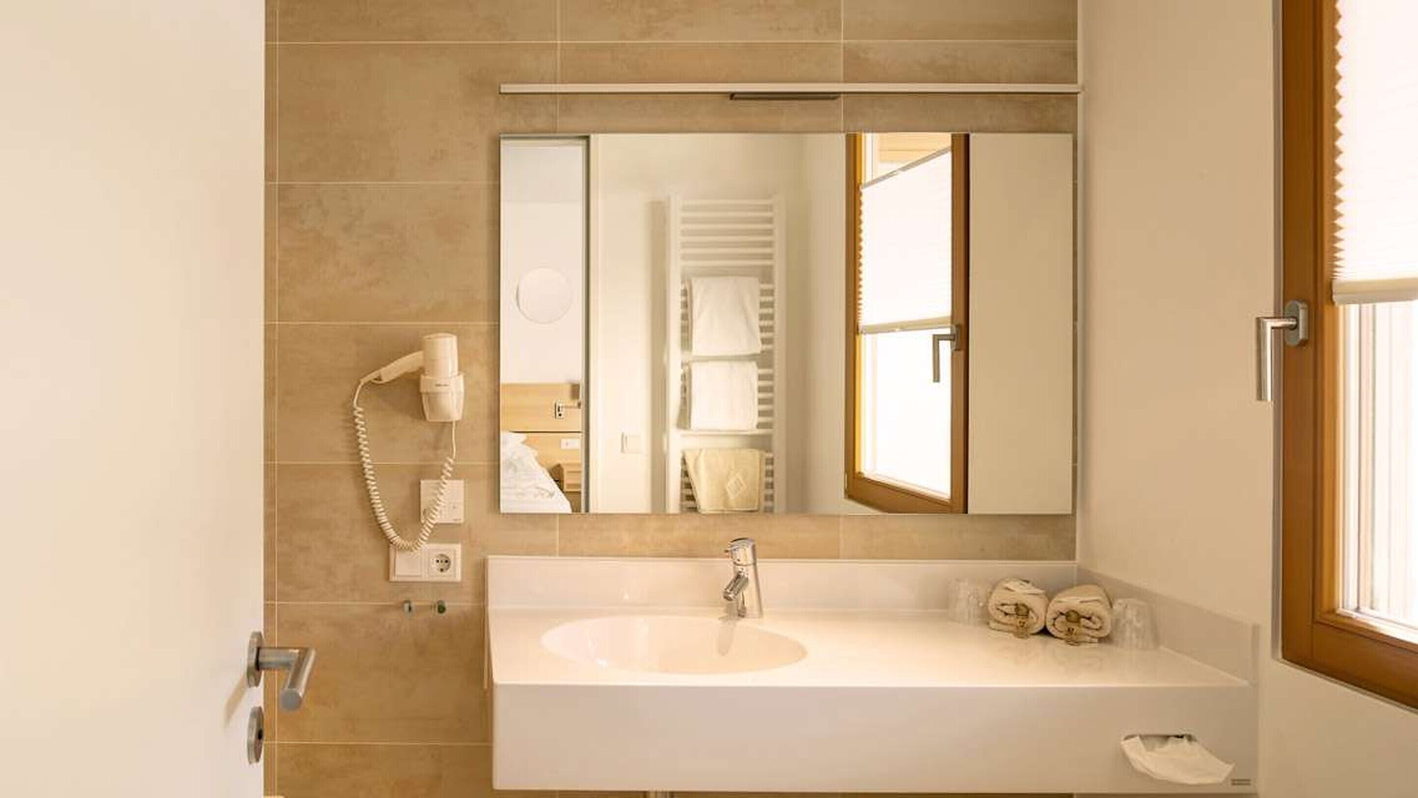 A bathroom with a large mirror, a sink, a hairdryer, and a towel rack.