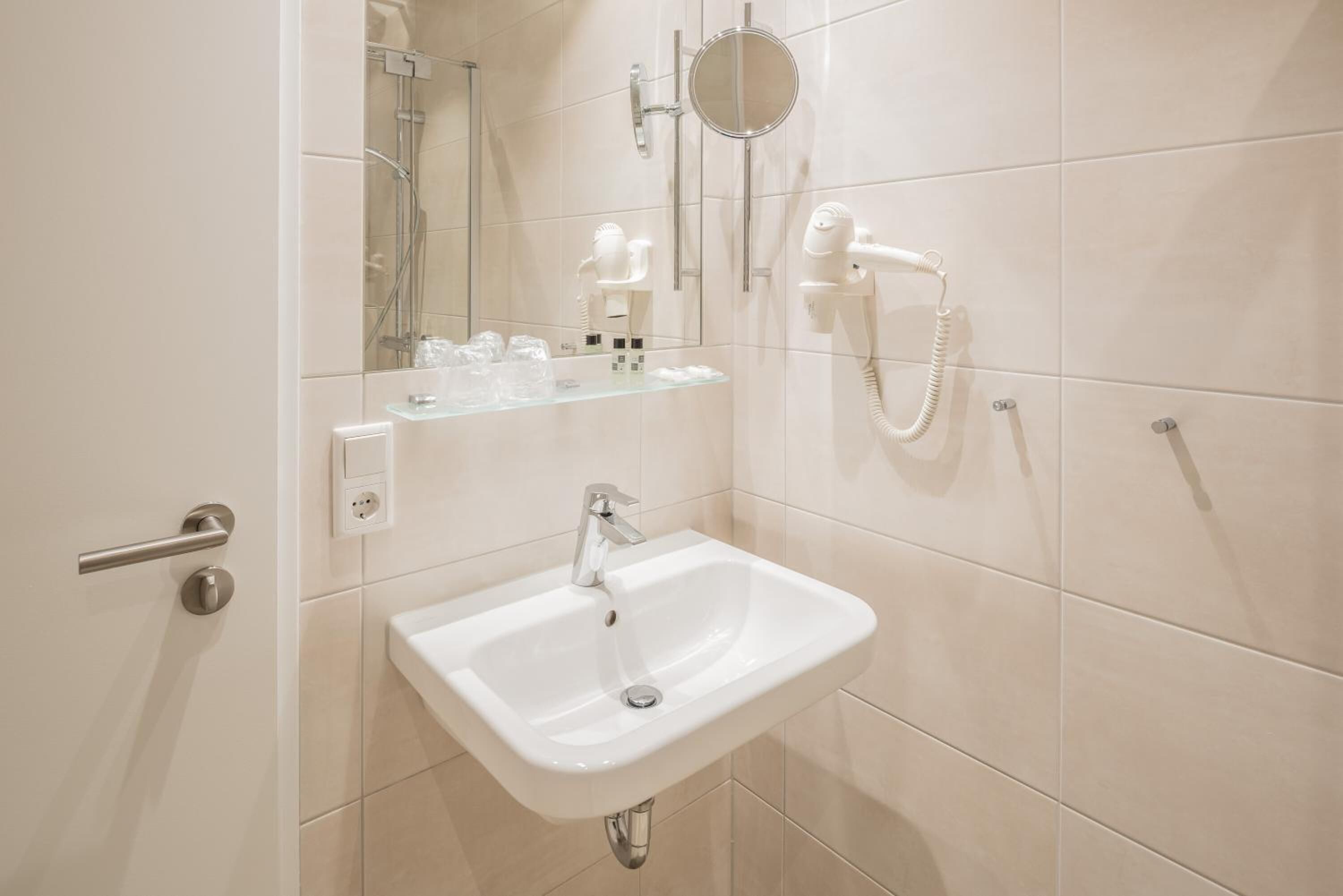 A bathroom with a white sink, a mirror, a handheld showerhead, and a hairdryer.