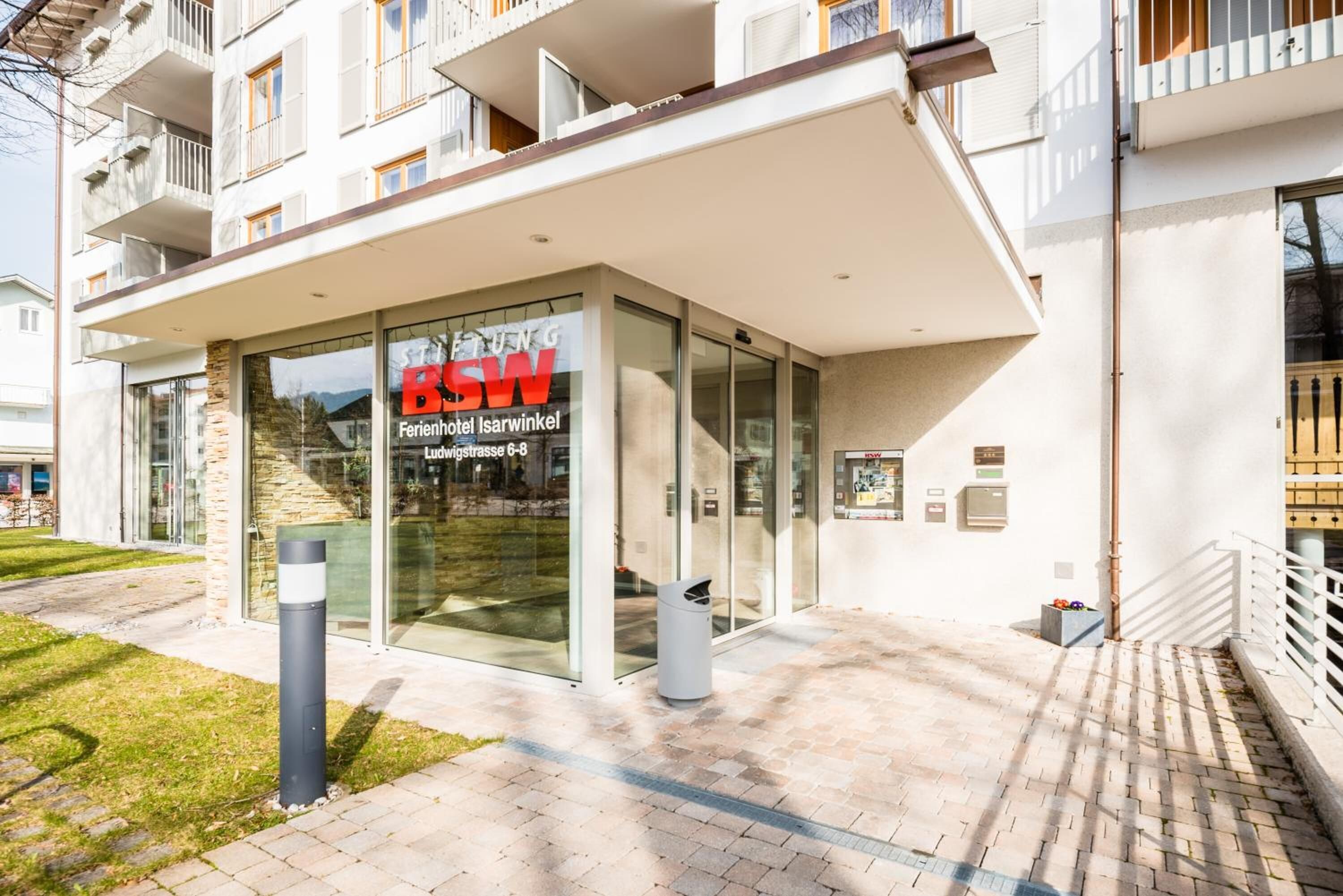 Une entrée d’hôtel moderne avec une façade en verre, une plaque signalétique et un chemin d’accès dégagé menant à l’entrée.