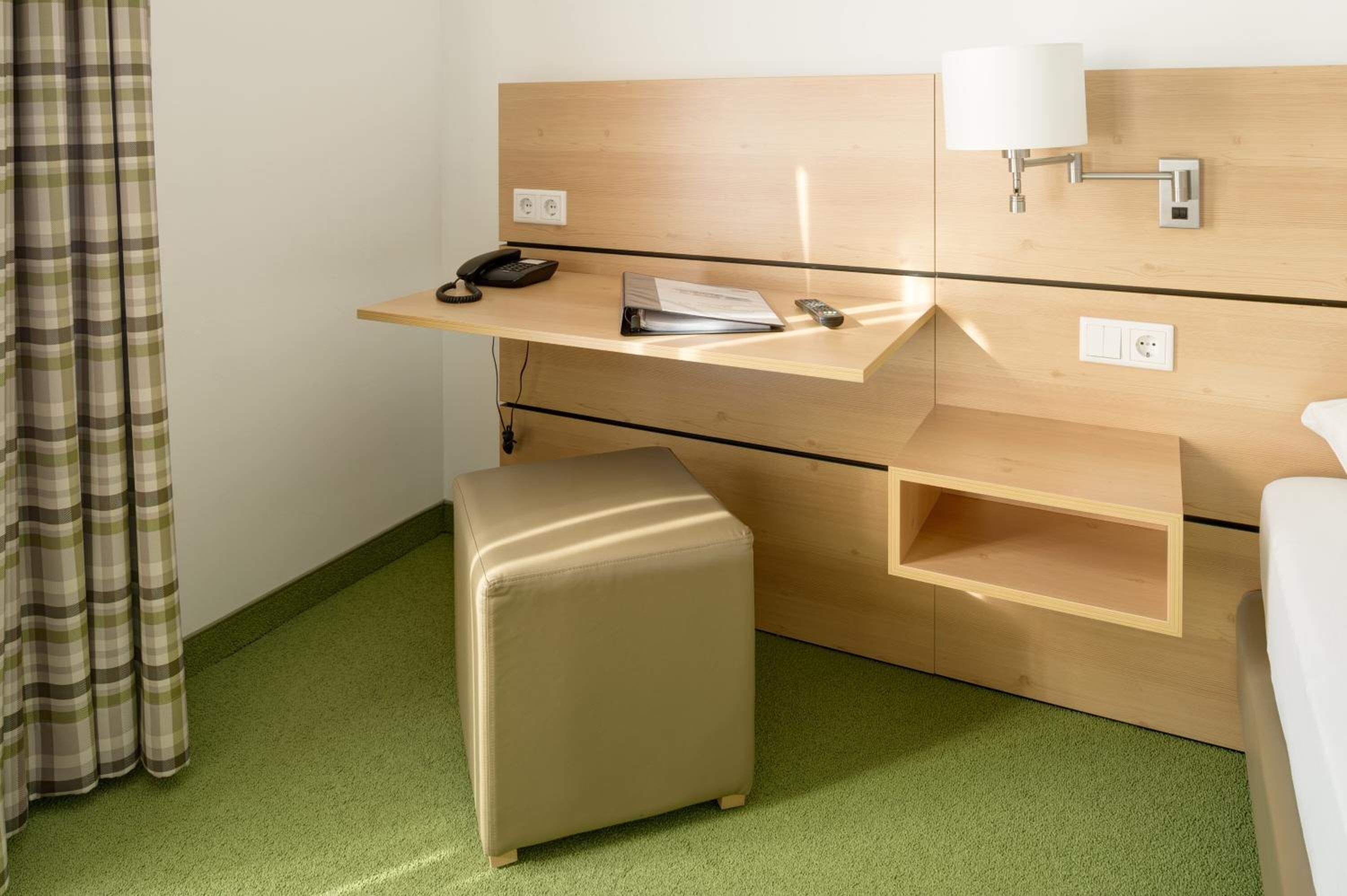 Een hotelkamer met een houten bureau, een telefoon, een lamp en een klein voetenbankje.