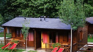Una cabaña de madera con un porche, dos sillones rojos y una mesita.