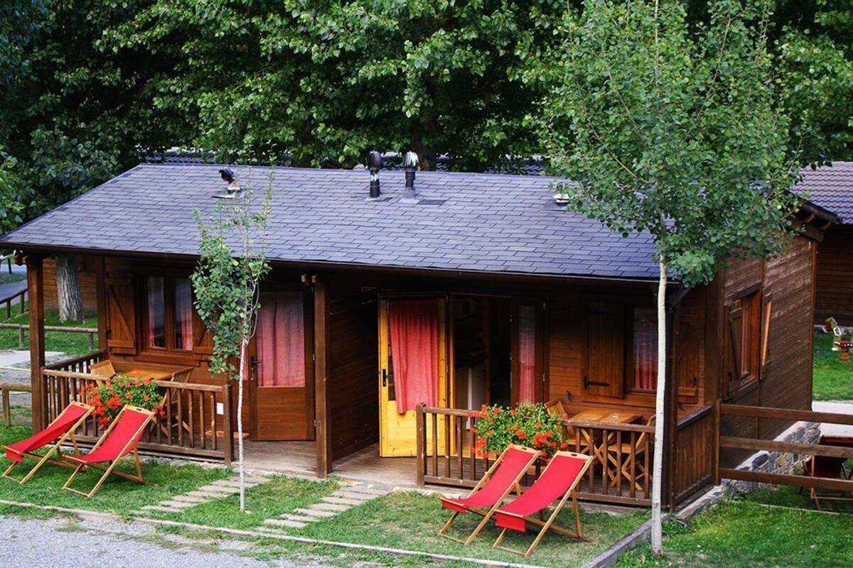 Una cabaña de madera con un porche, dos sillones rojos y una mesita.