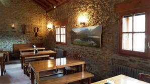 Un comedor rústico con bancos y mesas de madera, paredes de piedra y un cuadro de un paisaje montañoso.