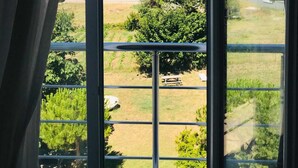 A room with a large window overlooking a grassy area with trees and a distant view of the sea and buildings. - Boss II Hotel (Eceabat)