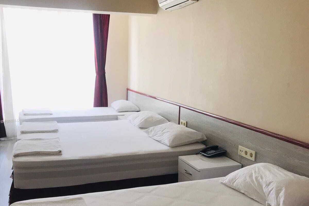 Hotellihuone, jossa on kolme sänkyä, yöpöytä, jossa on puhelin, ja ilmastointilaite seinällä.