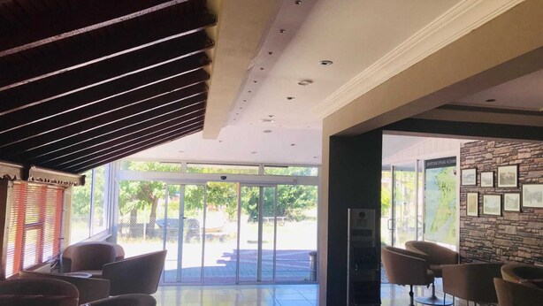 A hotel lobby with a glass door entrance, a seating area with chairs, a stone wall with framed pictures, and a ceiling with recessed lighting. - Boss II Hotel (Eceabat)