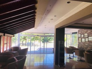 A hotel lobby with a glass door entrance, a seating area with chairs, a stone wall with framed pictures, and a ceiling with recessed lighting. - Boss II Hotel (Eceabat)