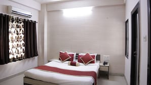 Habitación de hotel con cama, mesita de noche, unidad de aire acondicionado y ventana con cortinas estampadas.