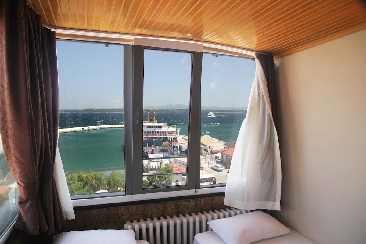 A room with a large window overlooking a port, a bed, and a radiator.