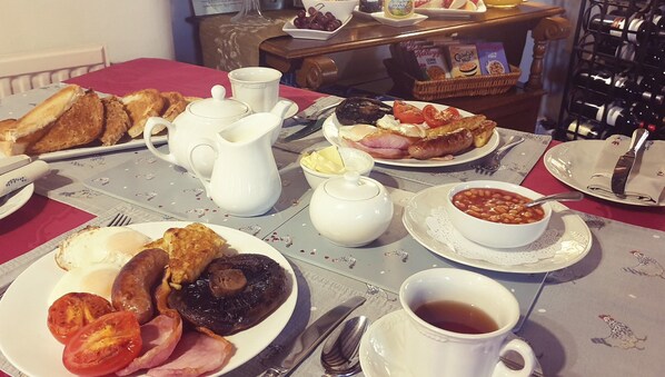 A breakfast table with plates of eggs, bacon, tomatoes, and sausages, a jug of milk, a cup of tea, and a bowl of beans. - Dannah Farm Country House (Belper)