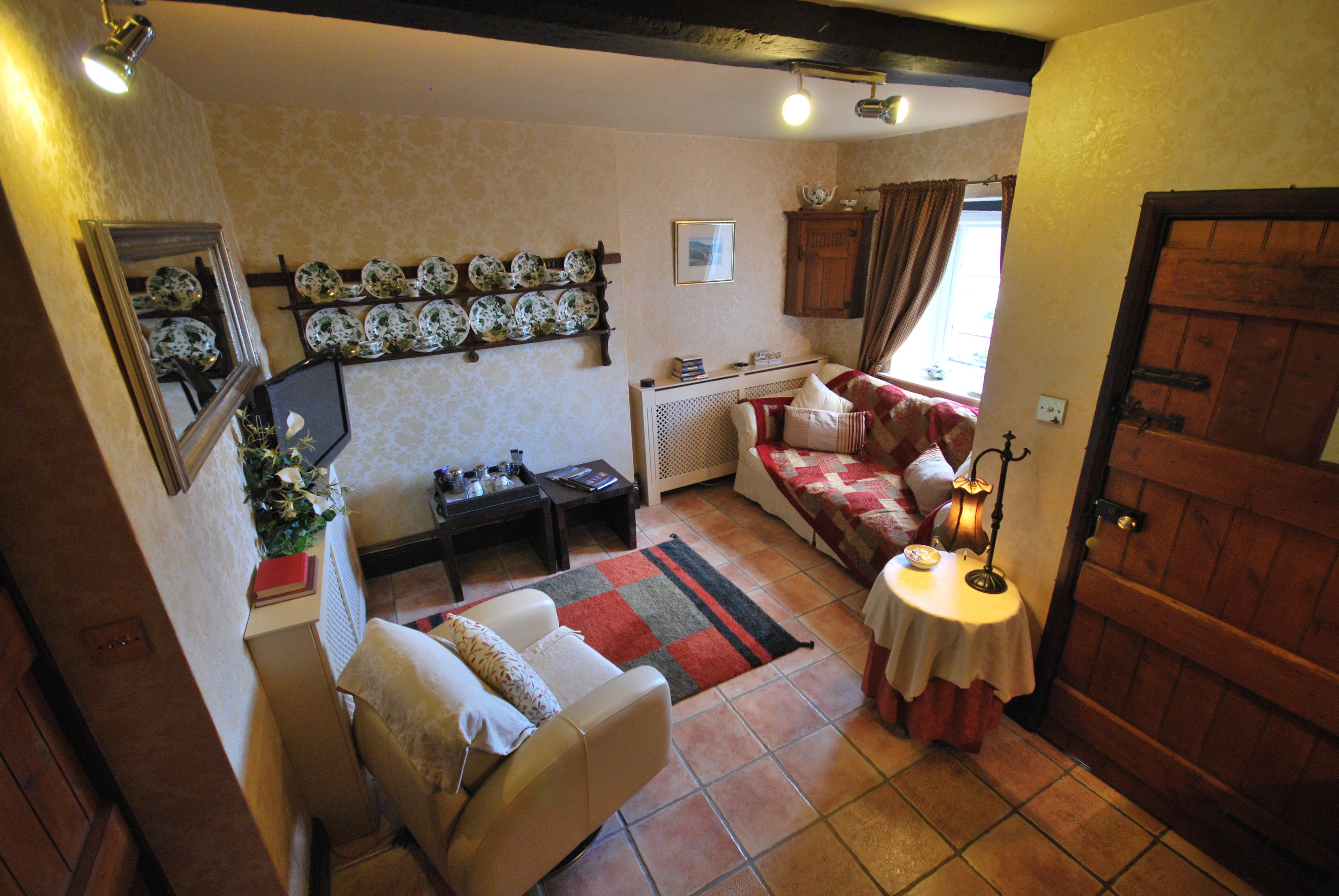 A cozy room with a bed, a chair, a table, and a shelf with plates.
