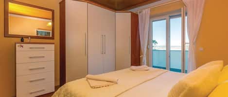 A bedroom with a bed, a wardrobe, a mirror, and a view of the sea through a window.