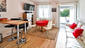 A modern living room with a wooden dining table, white chairs, a red tablecloth, a sofa with red cushions, a TV mounted on the wall, and a sliding glass door leading to an outdoor area. - Nice apartment in Dramalj with WiFi (Dramalj)