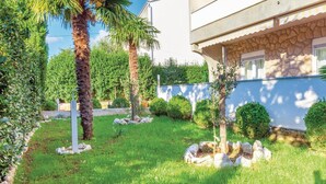A well-maintained garden with palm trees, neatly trimmed bushes, and a stone wall. - Nice apartment in Dramalj with WiFi (Dramalj)