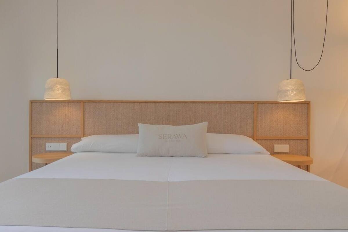 Una cama bien hecha con un almohadón que dice "SERAWA" y un cabecero de madera.