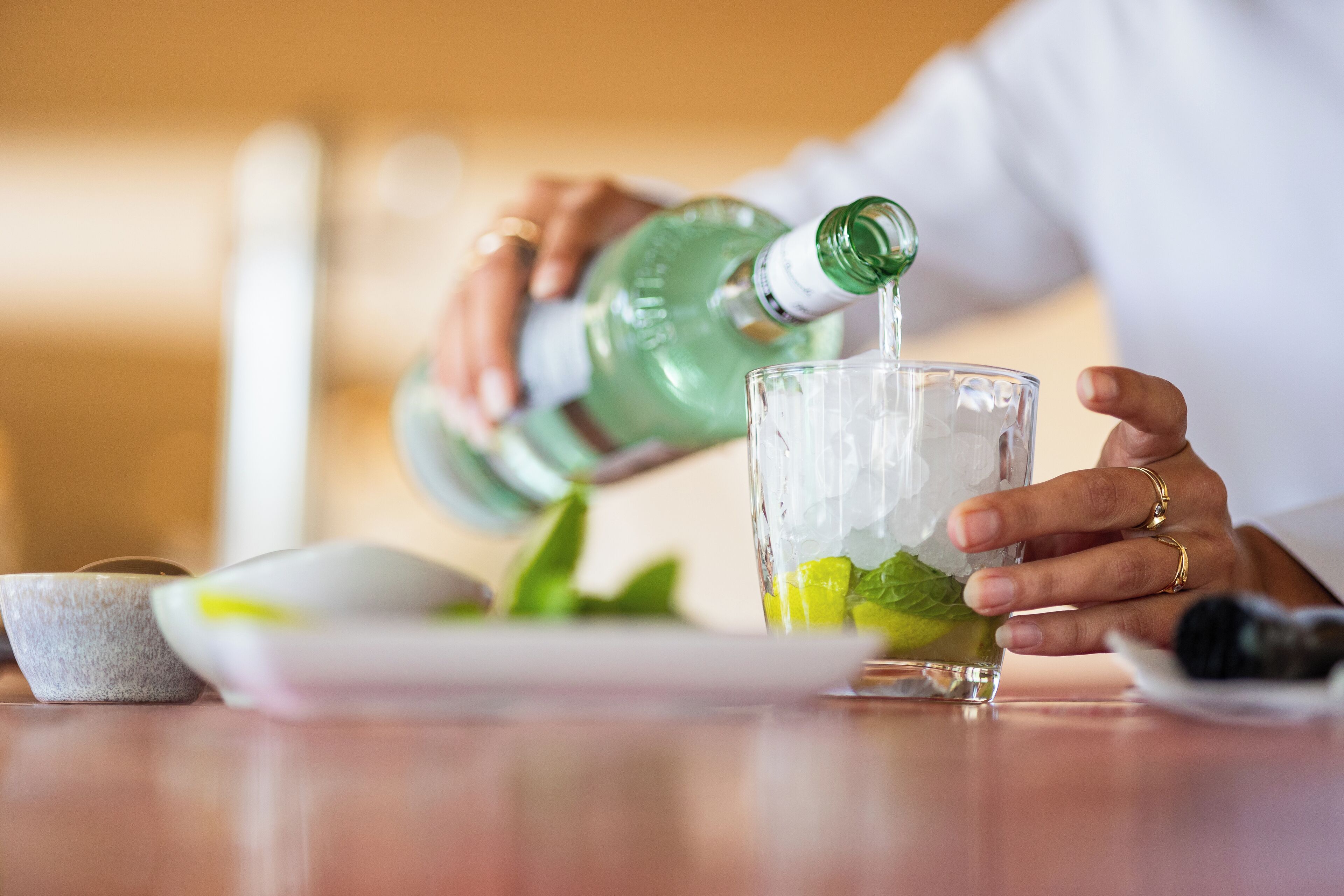 Une personne verse un liquide vert dans un verre contenant des glaçons et des feuilles de menthe.