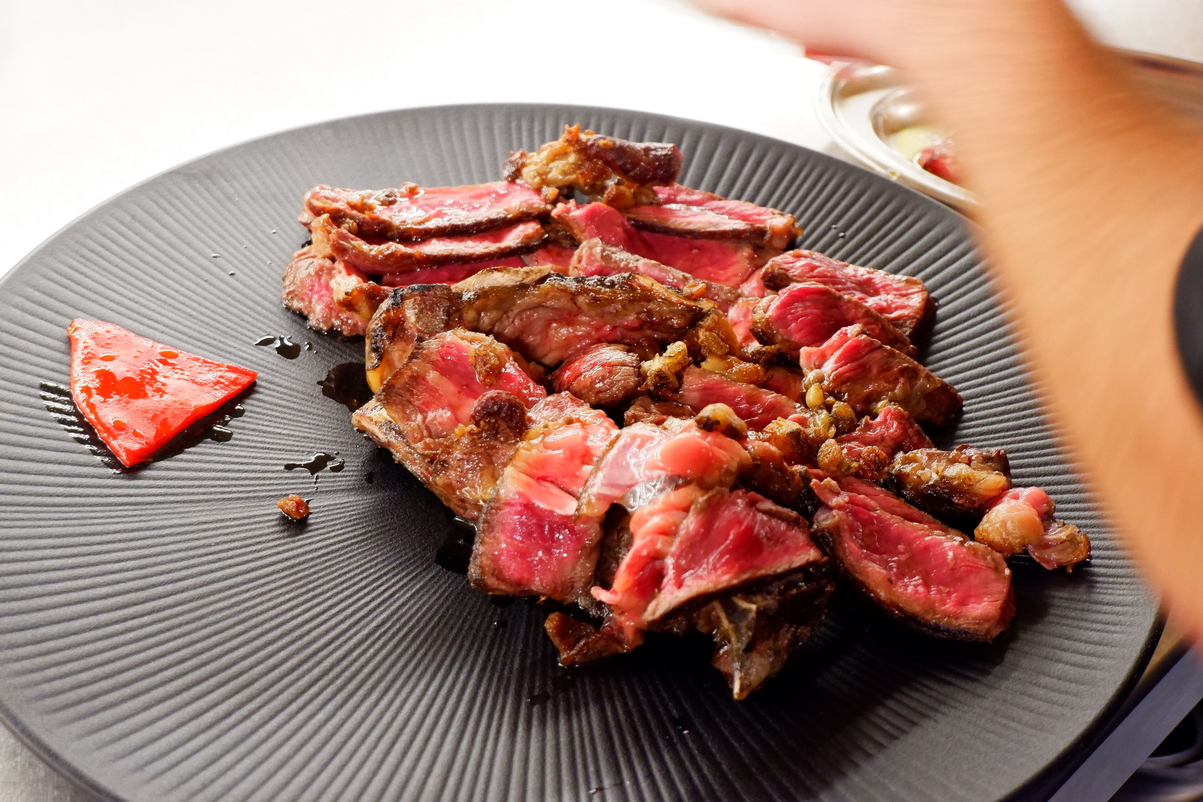 Un plato de filete en rodajas con guarnición roja sobre un plato negro texturizado.