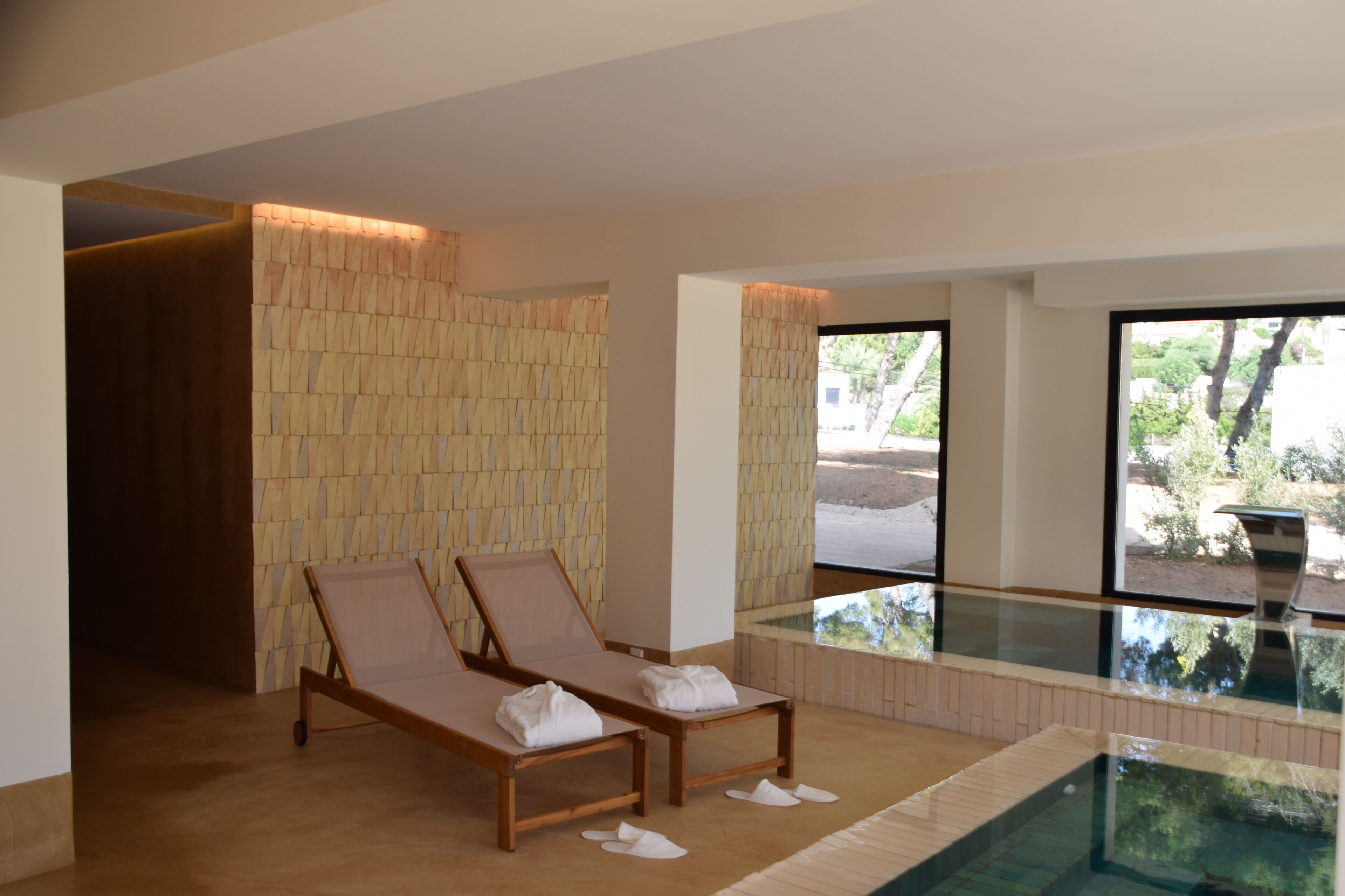 A spa area with two wooden loungers, a glass-enclosed hot tub, and a stone wall.