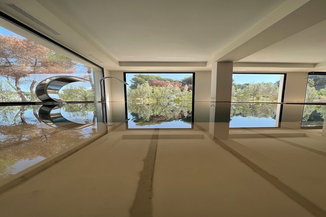 Un interior moderno con amplios ventanales que reflejan árboles y un cielo despejado.
