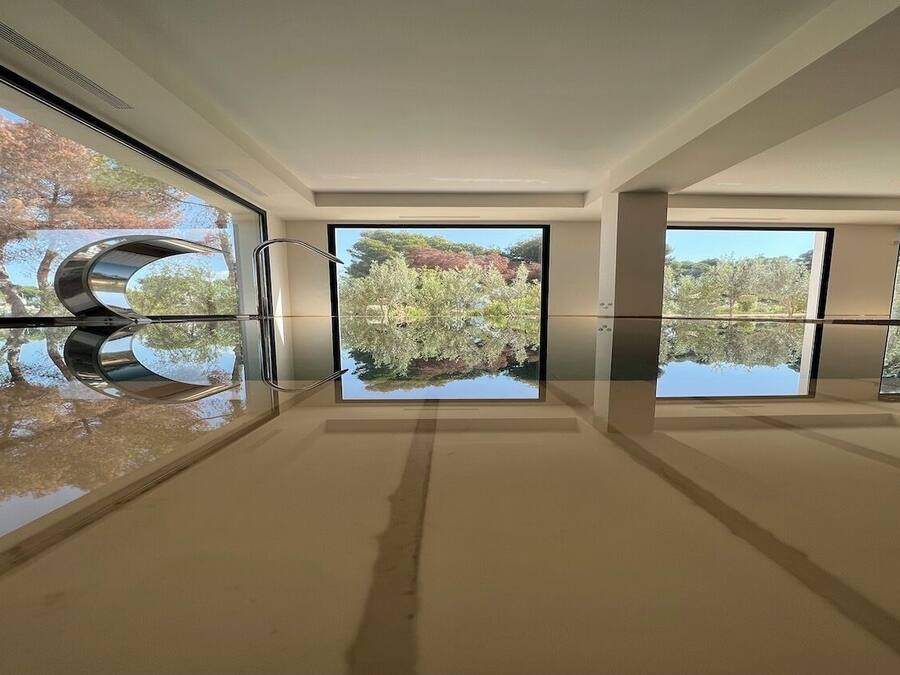 Un interior moderno con amplios ventanales que reflejan árboles y un cielo despejado.