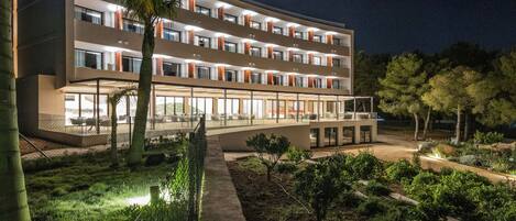 Un hotel de varios pisos con un diseño moderno, con balcones y un exterior bien iluminado.