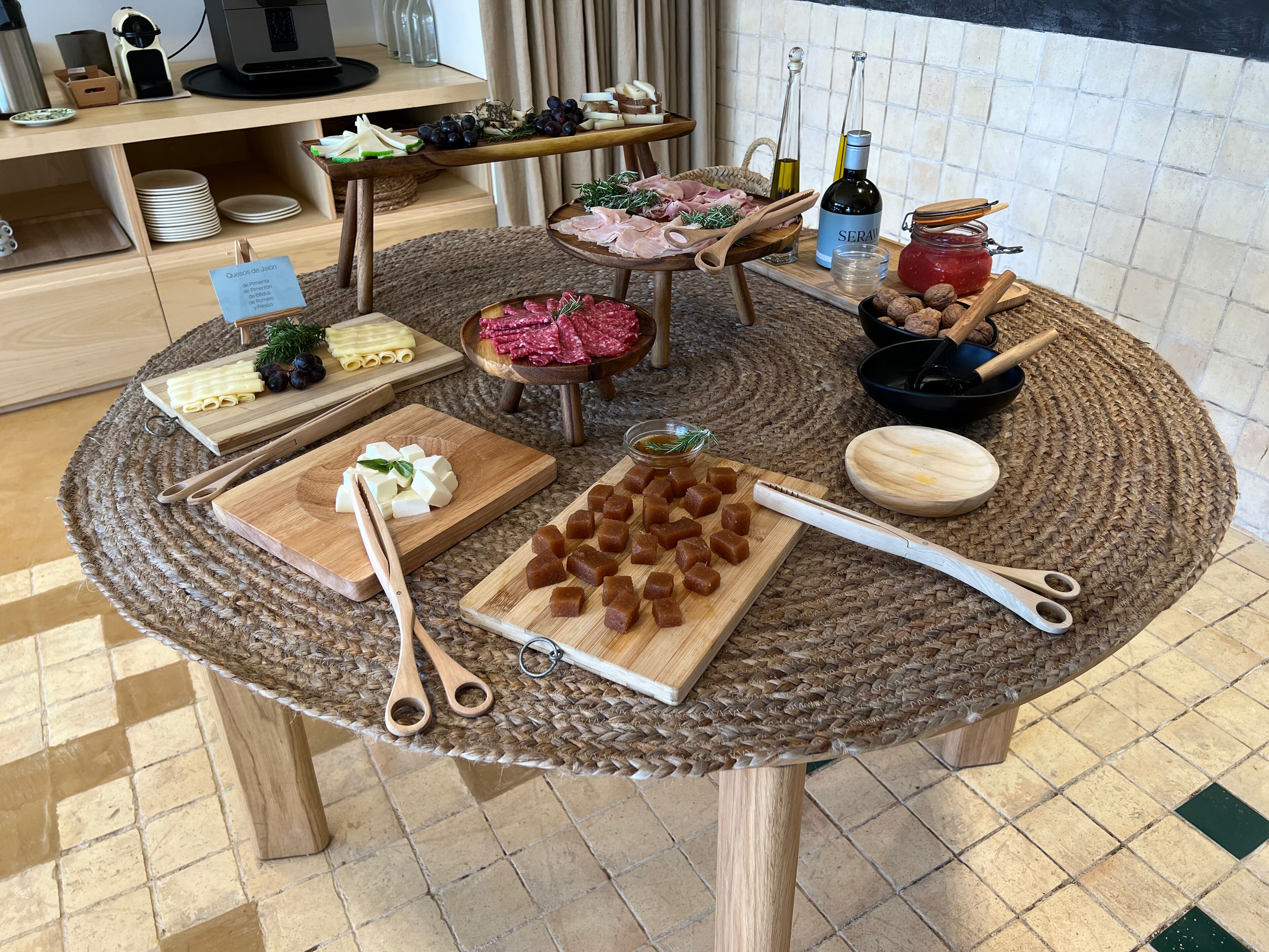 A round wooden table with various food items and utensils, surrounded by a woven placemat.