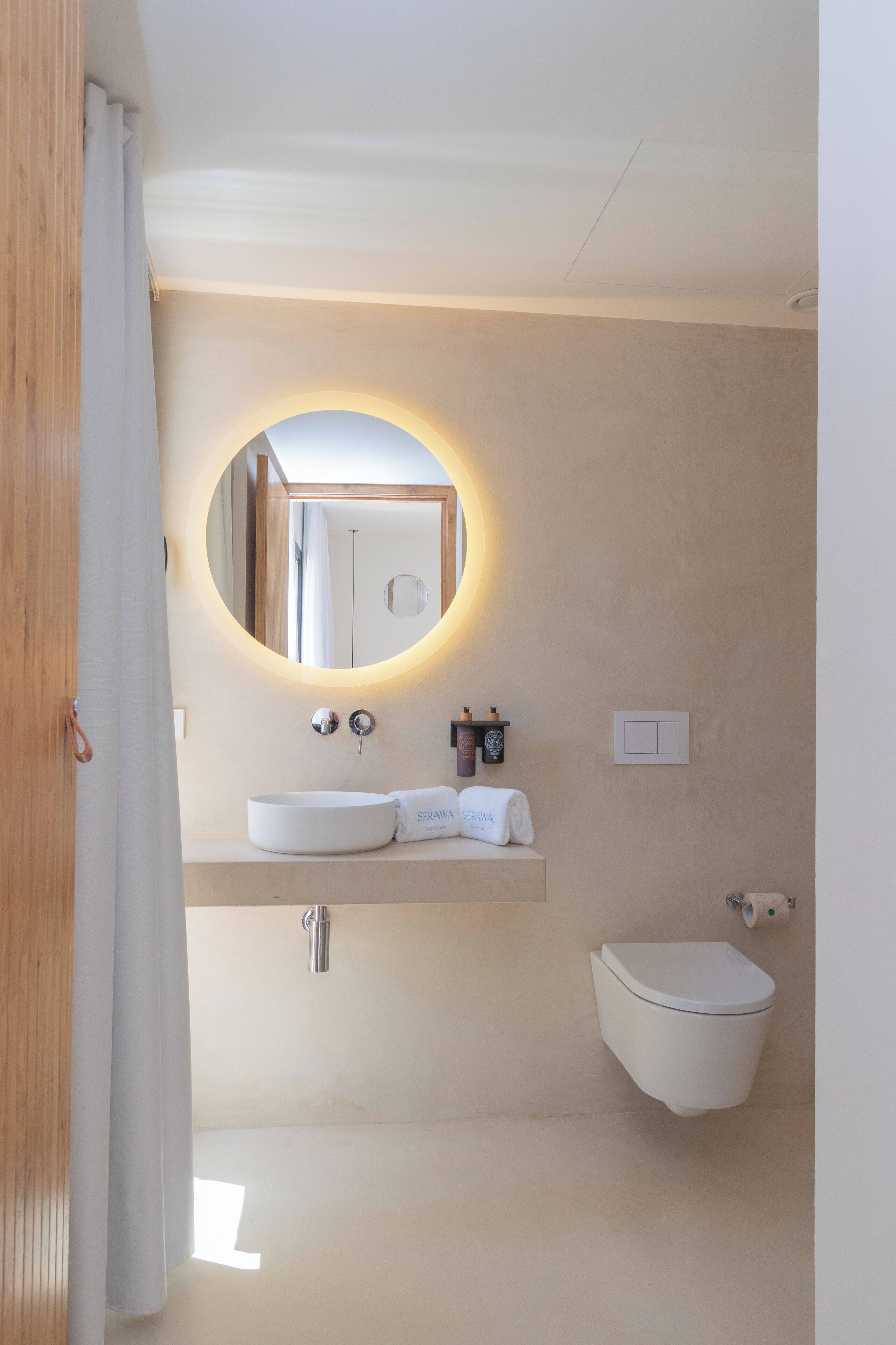 Et moderne badeværelse med et rundt spejl, en hvid vask og et toilet.